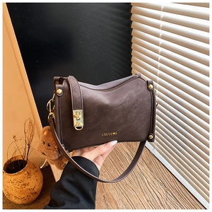 Detail der dunkelbraunen Lederhandtasche mit goldenem Logo und einem Plüschbär-Anhänger