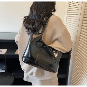 Detailed view of black faux leather tote with decorative bow and logo on a model