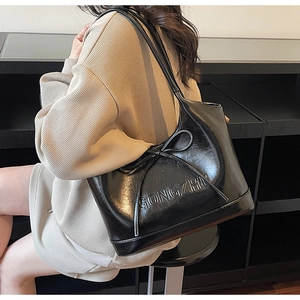 Détail du sac bandoulière noir brillant avec nœud 3D et gaufrage sur la finition laquée