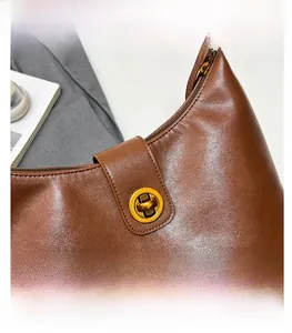 Close-up of a brown leather shoulder bag with a gold circular twist lock detail