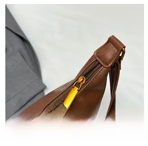 Detail showing the smooth gold metal zipper and stitching on a brown leather shoulder bag