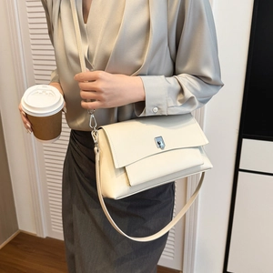 Close-up of beige leather crossbody bag with silver square lock worn by a model