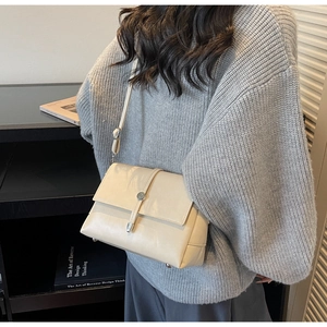 Detail of an ivory crossbody bag showing the metallic cylindrical buckle and flap closure