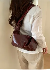 Close-up of elegant burgundy crescent bag in glossy leather worn by a female model