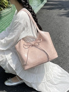Pink faux leather shoulder tote bag with a large bow detail shown in an outdoor setting