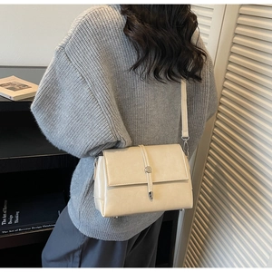 Detailed view of a cream leather crossbody bag with round metallic clasp on a model
