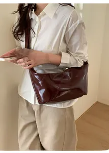 Detail of dark burgundy patent leather shoulder bag with diagonal stitching on model
