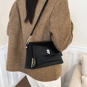Close-up of a black leather crossbody bag with a silver square clasp worn with a tweed jacket