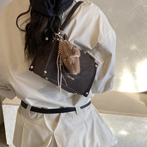 Detail einer dunkelbraunen Retro-Umhängetasche mit Goldnieten und Plüschbär-Anhänger