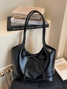 Glossy black leather tote bag with bow detail and GONGZHU embossing on artistic background