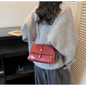 Deep red leather crossbody bag detail showing structured shape and metal buckle on strap