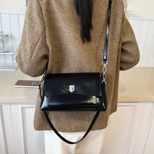 Detail of a black glossy leather crossbody bag paired with a brown wool suit jacket