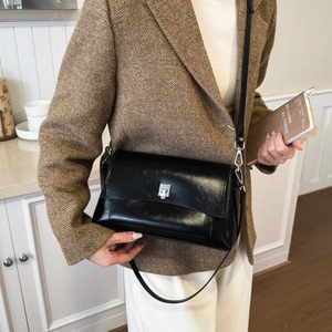 Close-up of a vintage black glossy leather crossbody bag with silver buckle on a model