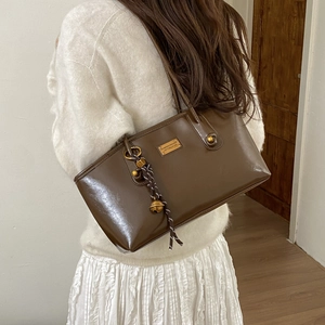 Detalle del bolso de hombro marrón brillante con amuleto de campana y metal dorado