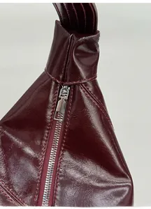 Detail of high-gloss burgundy leather bag featuring a robust silver metal zipper close-up