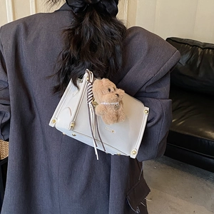 Detailansicht einer beigen Leder-Umhängetasche mit Plüschbär-Anhänger und Gold-Ecken