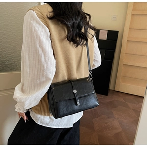 Detail of black crossbody bag with silver metal buckle on a stylish minimalist outfit
