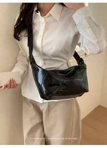 Detail of minimalist black patent leather crescent bag with pleated texture on model