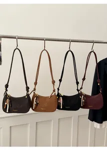 Détail de quatre sacs demi-lune en cuir avec pompons en perles et lettrage doré élégant