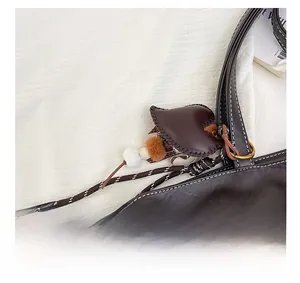 Detail of dark brown leather tote with heart charm and bicolor woven strap