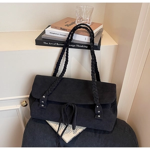 Detail of black suede tote bag featuring handcrafted woven strap and bow tie closure
