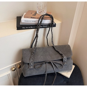 Close-up of grey suede shoulder bag with woven strap, metal rivets and bow detail