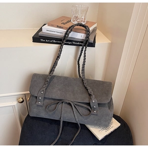 Detail of dark grey suede shoulder bag featuring braided strap and elegant bow detail