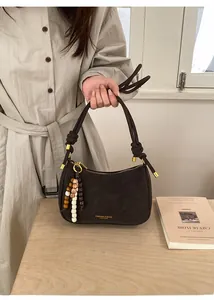 Détail du sac demi-lune en cuir marron foncé avec breloque en perles et poignée nouée