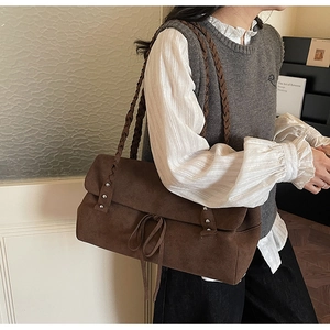 Detail view of brown suede handbag featuring braided shoulder strap and metallic rivets