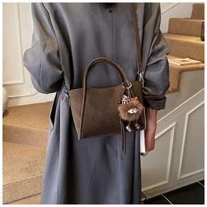 Dettaglio borsa a secchiello marrone con ciondolo leopardato su modella in cappotto grigio
