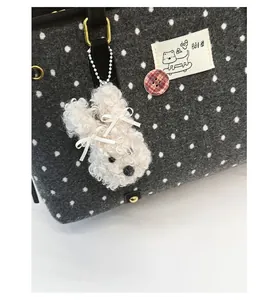 Detail view of a white plush charm with satin bows on a grey polka dot tote bag