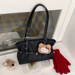 Detail of black leather tote bag with metal eyelet straps and plush bear charm