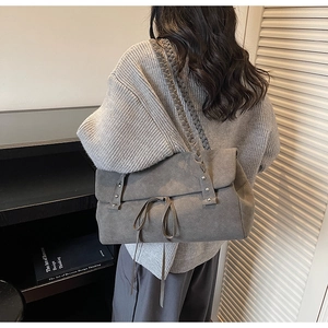 Detail of grey suede shoulder bag featuring woven straps and metallic rivet accents
