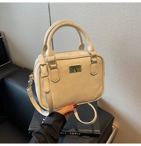 Detail of creamy white leather crossbody bag with dual handles and gold metal hardware