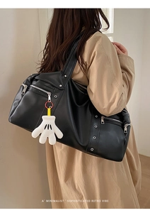 Detail of a black retro biker shoulder bag featuring silver zippers and a white charm