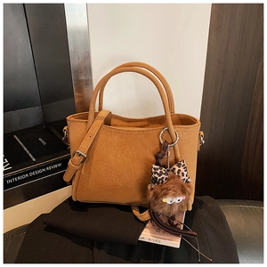 Detail view of tan leather small square bag with plush leopard bow charm on desk