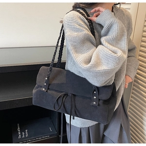 Detail of black suede shoulder bag with chunky woven strap and metallic rivet accents