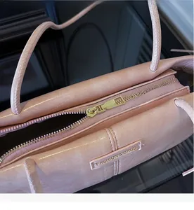 Detail of pink faux leather shoulder bag featuring smooth gold metal zipper and logo plaque