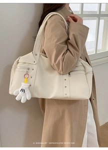 Detail of off-white travel bag with silver studs and a plush glove pendant on shoulder