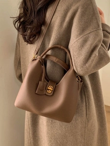 Braune Beuteltasche aus Leder mit Tragegriff und Goldverschluss an Wollmantel-Model