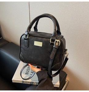 Detailed view of black textured Boston handbag with gold metal plate on decorative books