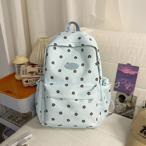 Detail of light blue floral backpack with front zipper pocket and side pockets in a home setting