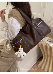Detail of a large dark brown leather travel bag with vintage studs and plush charm