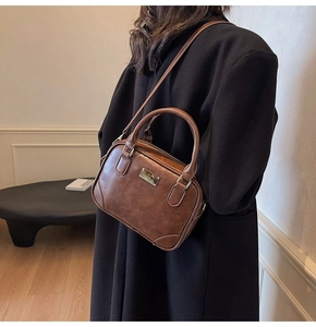 Detail of vintage brown leather handbag with cylindrical handles and metal plate ornament