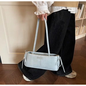 Detail of light blue bow baguette bag with side tassel and fashion logo displayed by model