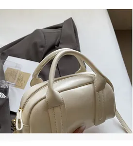 Sac à main Boston blanc crème exposé avec un livre d'art et un blazer gris, style minimaliste