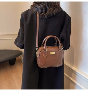 Brown vintage faux leather square handbag worn over a black coat in a cozy room