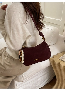 Détail du sac demi-lune en daim bordeaux avec bandoulière nouée et perles en bois