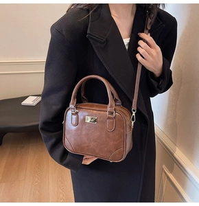 Close-up of brown vintage leather crossbody bag with gold metal plate on a black coat