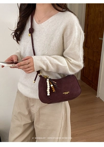 Détail du sac bandoulière en daim bordeaux avec pompon perlé et garniture dorée élégante